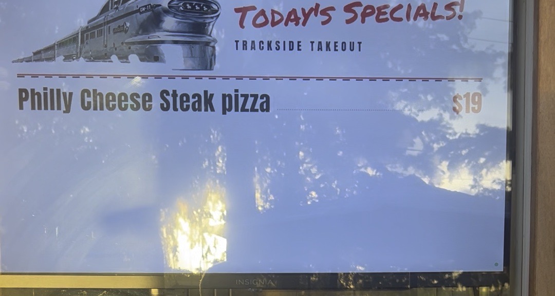 Photo through Trackside Takeout's front window of their TV showing Today's Specials.